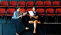 two students run script lines while sitting in red theater seats