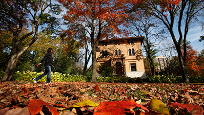 Rich fall colors of orange and red surround a student walking past the Annie Mae Swift building