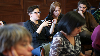 Female student with short hair and black glasses speaks in a room full of other students