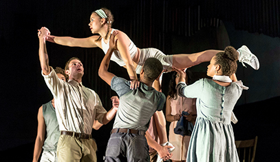 Three student performers rehearse a play by holding a female student overhead in Superman pose