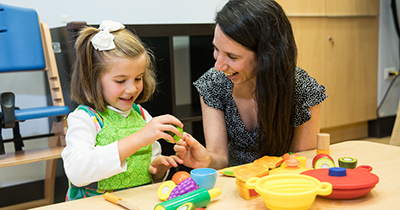 Smiling women works with happy young girl at table full of colorful blocks 