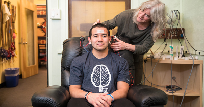Neurobiology professor adjust brain sensors on the head of a student sitting in comfortable chair