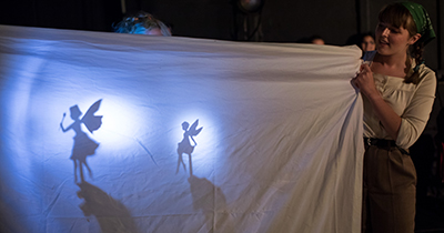 Two hand-held cutouts of winged fairies create dramatic shadows large white sheet